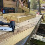 Home Close-up of carpentry work on a deck with a nail gun and wooden frame under construction.