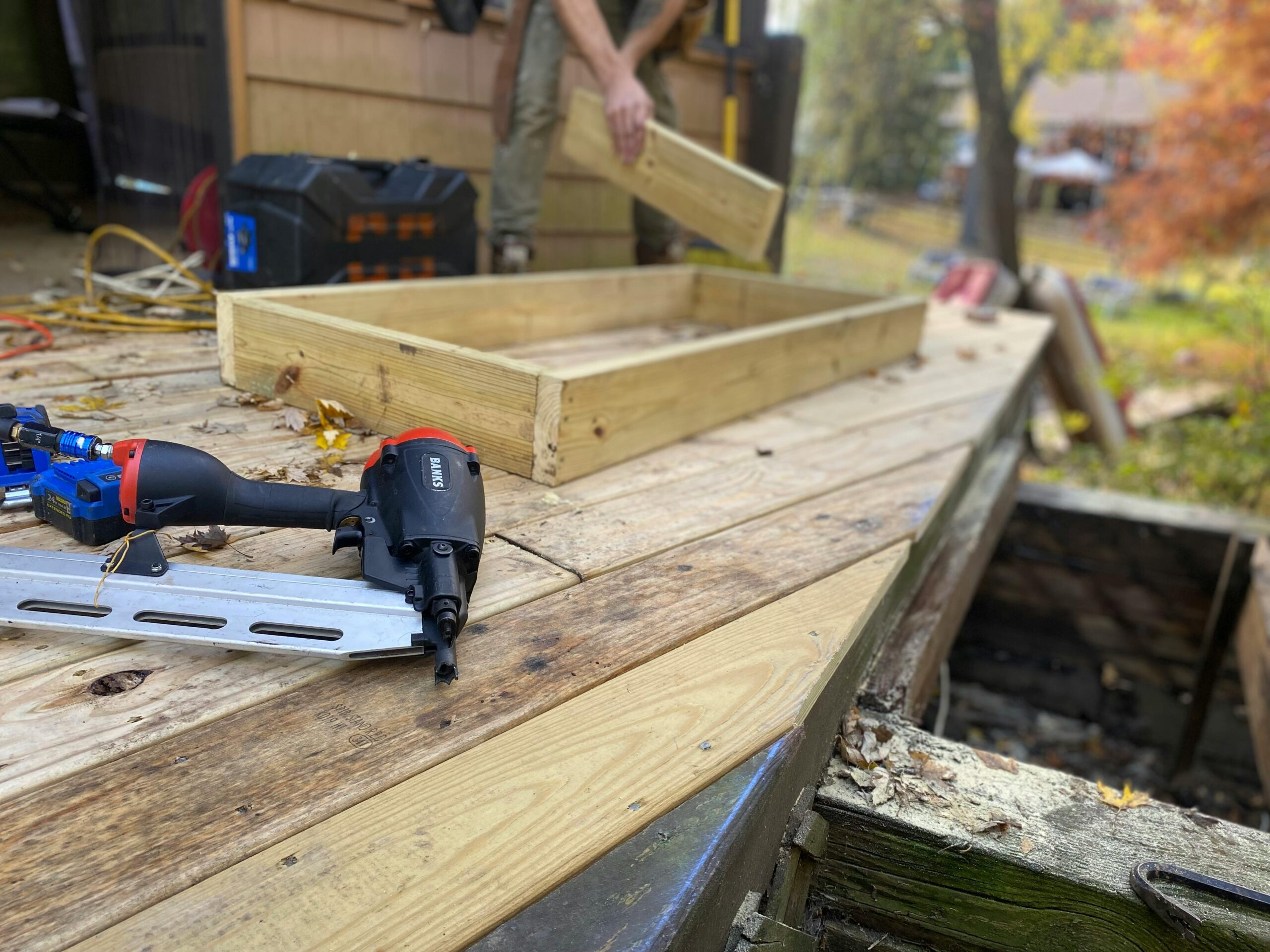Home Close-up of carpentry work on a deck with a nail gun and wooden frame under construction.