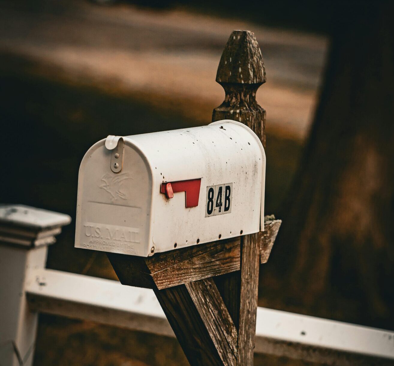 Home Old-fashioned white mailbox on a wooden post, creating a vintage feel in a rural setting.