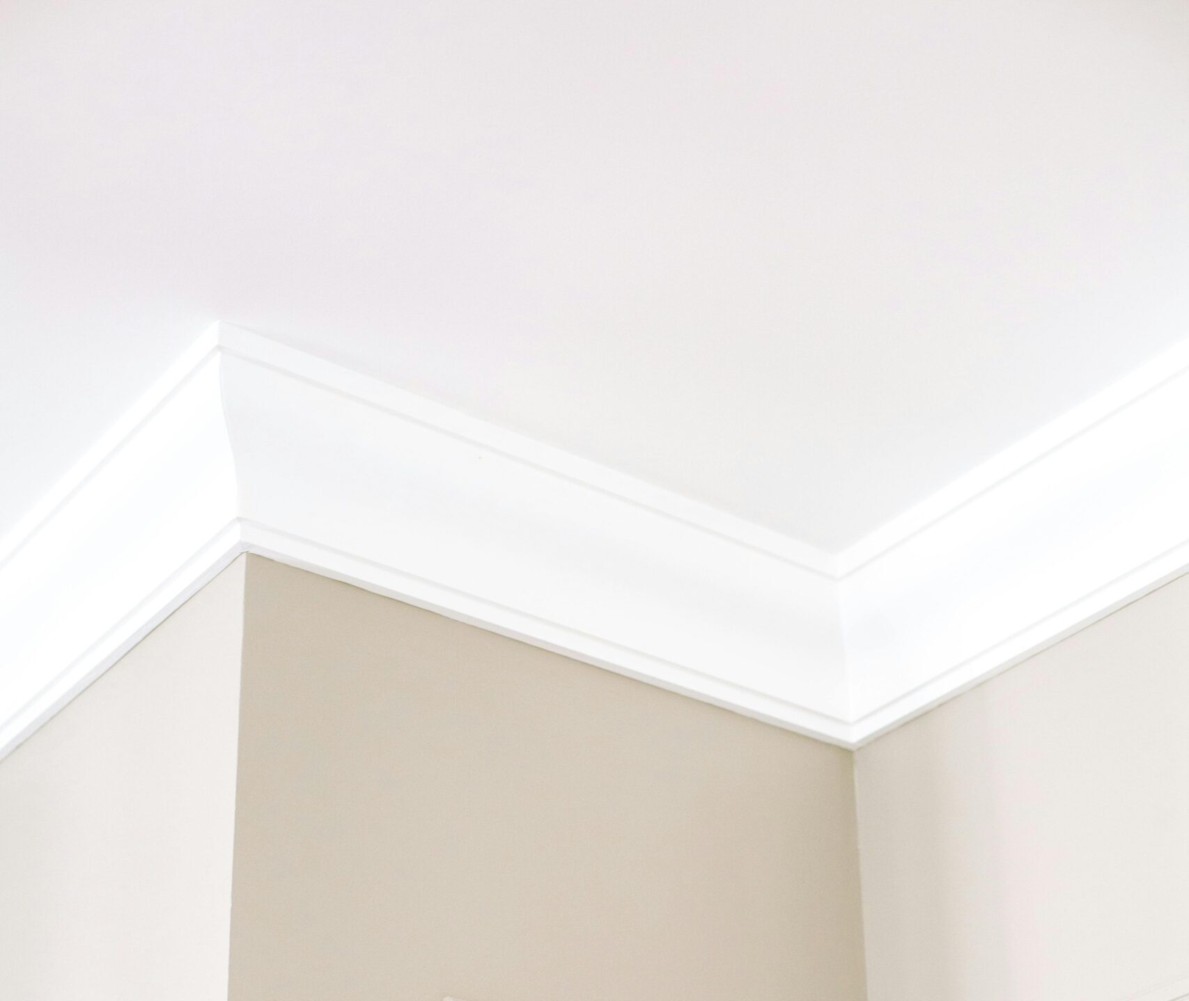 Home Close-up of intricate ceiling moulding and beige walls with minimalist design, showcasing home renovation details.