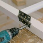 Home Close-up of an electric drill installing a door hinge on a wooden workbench.